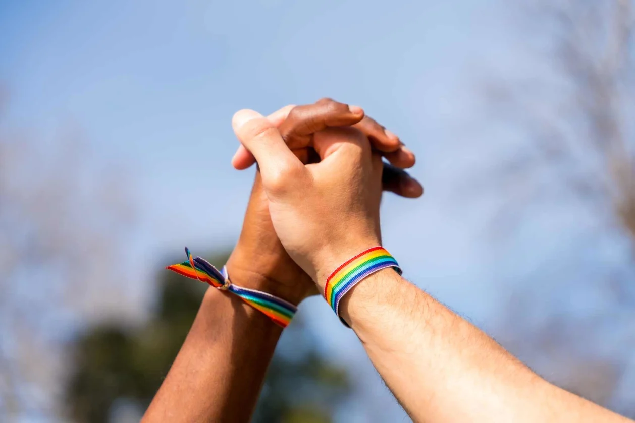 two men holding hands with pride bracelets